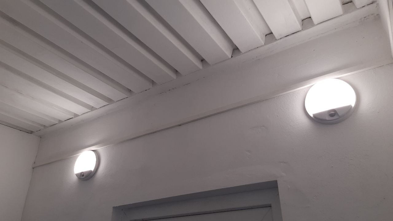Dvě rozsvícená nástěnná LED svítidla pod dřevěným stropem