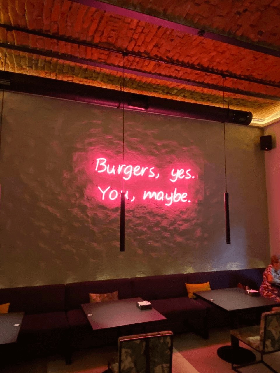 Neonový nápis Burgers, yes. You, maybe. nad sedací soupravou